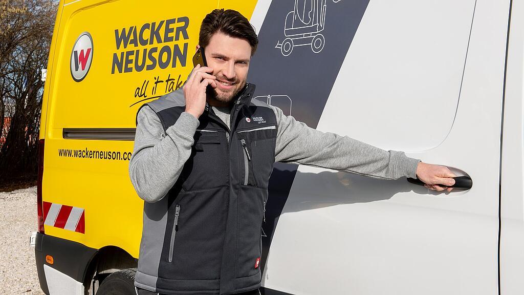 Zamestnanec Wacker Neuson stojí pred servisným vozidlom Wacker Neuson a telefonuje.