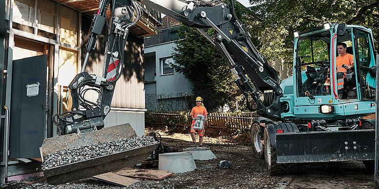 Kolesové rýpadlo Wacker Neuson EW100 manipuluje na stavenisku s sypkým materiálom pomocou sklopnej lopaty.