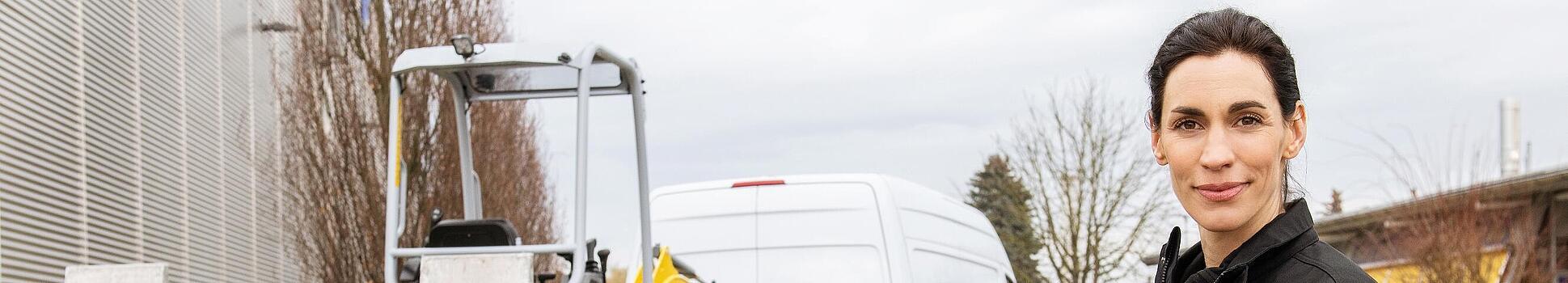 Zamestnankyňa Wacker Neuson stojí pred pásovým rýpadlom Wacker Neuson na prívese.