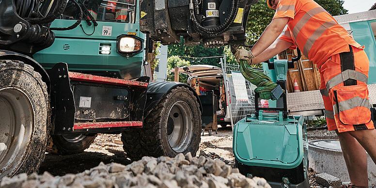 Operátor vymieňa príslušenstvo na kolovom rýpadle Wacker Neuson EW100 počas prác na stavenisku.