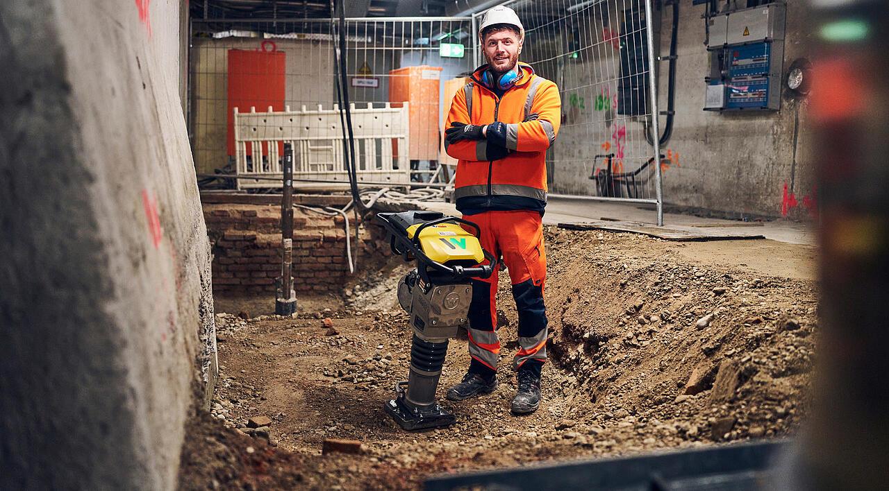 man standing next to battery powered rammer from wacker neuson at construction site